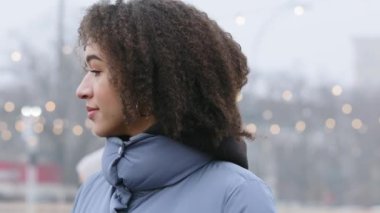 Portet dalgın üzgün, odaklanmış Afrikalı Amerikalı kız kışın açık havada dikilip erkek arkadaşını beklerken koyu tenli, yalnız, ciddi, genç bir kadın yüzü ifadesi takınıyor.