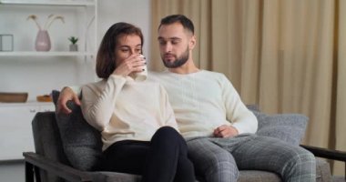 Kafkasyalı genç bir çift modern kanepede, rahat oturma odasında oturan, çay içen bir kadın kahve içen bir adam hayal kuran bir adam, havada el hareketi gösteriyor.
