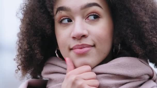 Töprengő fiatal etnikai nő 20-as éveiben áll a szabadban pózol néz félre úgy gondolja, jön ötletek dörzsölje az állát kézzel teszi döntés emlékszik fontos esemény a múlt mosolyok titokzatos — Stock videók