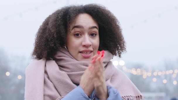 Porträt eines afroamerikanischen Mädchens mit lockiger Frisur fühlt sich kalt allein auf der Straße in der Stadt im Winter wärmt ihre gefrorenen Arme reibt Handflächen, um warm zu halten bringt Hände in den Mund pustet heiße Luft atmet Dampf — Stockvideo