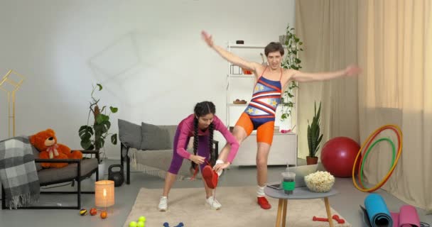 Kaukasischer großer lustiger Mann hilflos fauler Anfänger balanciert auf einem Bein, während Frauentrainer hilft, Schnürsenkel an Turnschuhen zu binden, Menschen in Retro-Sportbekleidung bereiten sich auf das Training vor — Stockvideo