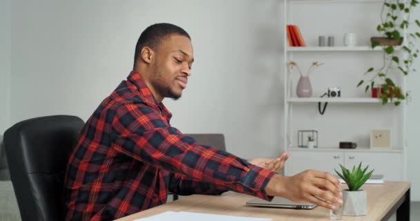 Afro mannelijke werknemer etnische zakenlieden zitten thuis kantoor sproeien antibacteriële ontsmettingsmiddel voor het ontsmetten van de behandeling handen voor het gebruik van laptop computer apparaat, veiligheid op het werk tijdens pandemie — Stockvideo