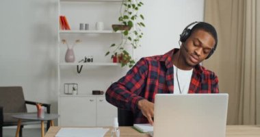 Komik, mutlu afro iş adamı kablosuz kulaklık takıyor iş yerinde molalarda müzik dinlerken eğleniyor. Siyahi besteci yazar, dizüstü bilgisayarla şarkı yazarak çevrimiçi uygulamada melodi yarattı.