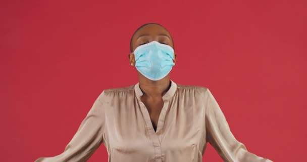 Retrato feminino em estúdio em fundo vermelho menina americana africana mulher calma usa máscara protetora médica durante coronavírus se livrar do medo e estresse medita faz entrar em pose respira profundamente — Vídeo de Stock