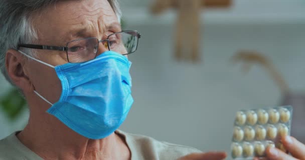 Tıbbi maske ve gözlüklü erkek yüzüne yakın çekim, yaşlı, hasta, gri saçlı adam büyükbaba acı belirtilerinden muzdarip, elinde ilaç paketi var. — Stok video