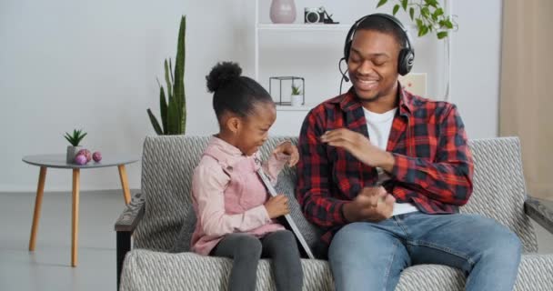 Μικρή αστεία κόρη κορίτσι διαλογίζεται με τον αγαπημένο της πατέρα Afro American μπαμπάς κάνει γονέα διάλειμμα για να χαλαρώσετε από το άγχος, ο άνθρωπος κατασκοπεύει εξαπάτηση κόρη φτάνει για φορητό υπολογιστή, εθισμό στην τεχνολογία — Αρχείο Βίντεο