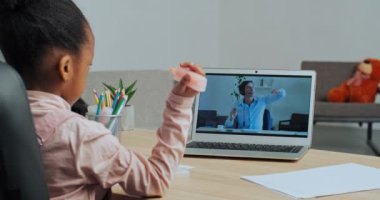 İnternet öğretmeniyle meşgul olan Afro-Amerikalı küçük kız öğrenci bilgisayarlı ekrandaki adamdan sonra çevrimiçi öğretmenle resim çizmeyi öğrendiği için evden video çağrısı yapıyor.