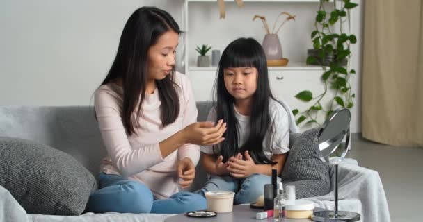 Genç anne Asyalı kadın ve küçük Koreli kız çocuğu koltukta oturup nemlendirici doğal losyon sürerek avuç içi güzelliği, insan ve sağlık kavramına el kremi sürerler. — Stok video