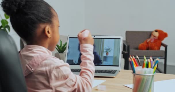 Pohled zezadu Afro americká malá školačka dcera sedí u domácího stolu čerpá s tužkami mluví ke své matce na on-line volání sledování video lekce od učitelky na notebooku, dálkové učení — Stock video
