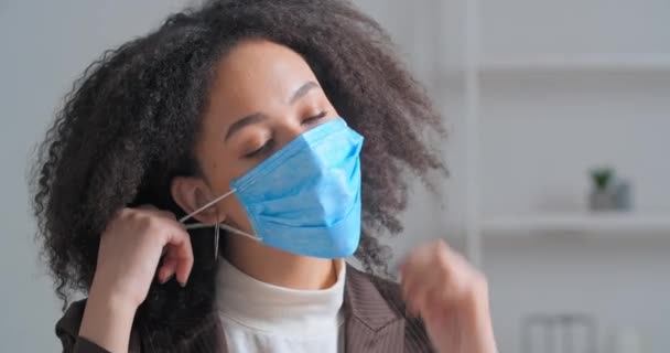 ポートレート悲しいアフロアメリカの巻き毛ビジネス女の子学生は彼女の医療面マスクを脱いで彼女の疲れを感じますハードデイワークプロジェクトはオフィスに座っている後、深く安堵ときれいな空気呼吸を必要とします — ストック動画