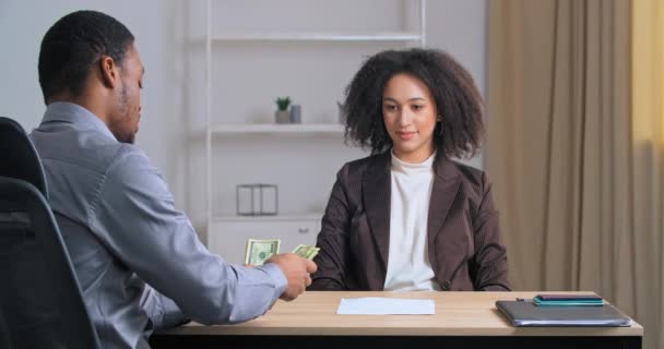 Афро-американський бізнесмен, який сидить за столом перед камерою, даючи професійній жінці грошову платню за добре виконану роботу потиснувши руки, партнерські фінансові відносини, хабар або концепцію продажу. — стокове відео