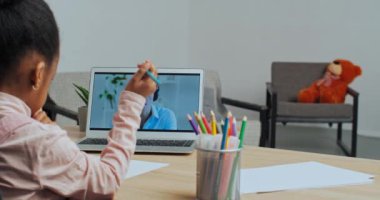 Tanımlanamayan küçük afro-amerikan okul kızı internetteki erkek öğretmen ekranına bakıyor. Karantina sırasında küçük kız resim çiziyor, e-öğreniyor.