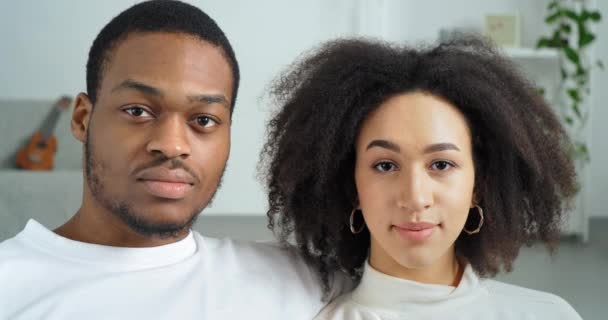Potret pasangan etnis serius afro muda keluarga american gadis keriting dan pria kulit hitam mengenakan pakaian putih kasual di rumah duduk bersama-sama dengan sangat melihat kamera dengan ekspresi wajah yang serius sedih — Stok Video