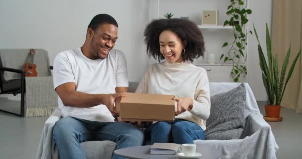 Афро-американская пара черный муж и жена покупатели покупатели получают посылку по почте из интернет-магазина с интересом открытой картонной коробке чувствовать удивление в подарок продукта, концепции доставки — стоковое видео