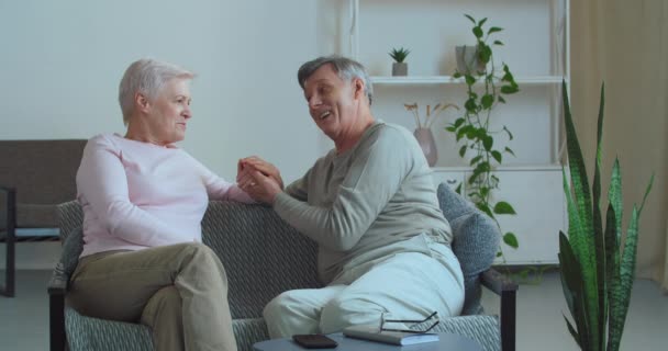 Europäische kaukasische glückliches älteres Ehepaar Familie von Rentnern alte Frau und älterer Mann sitzen auf der Couch in gemütlichem Haus mit ehrlichen, aufrichtigen Gesprächen Händchenhaltend, Zärtlichkeit Konzept — Stockvideo