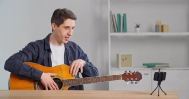 Kafkas erkek besteci öğretmen masada oturmuş cep telefonu kamerasına bakıyor. Karantina sırasında evden alınan gitar dersleri, insanlar ve yetenekleri anlatıyor.