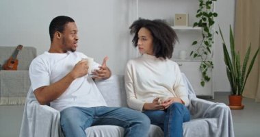 Afro-Amerikan çift, aile yakışıklısı erkek ve kıvırcık, çekici kız, evde gündelik giysiler giyip sabahları kanepede oturup sıcak kahve içip hafta sonları sohbetin tadını çıkarıyorlar.