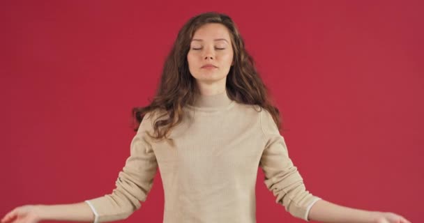 Studio portret jonge blanke vrouw kalm meisje het verhogen van de handen en mediteren op rode achtergrond. Zelfverzekerde slanke aantrekkelijke dame ontspannen met behulp van yoga meditatie staande in positie, evenwicht concept — Stockvideo