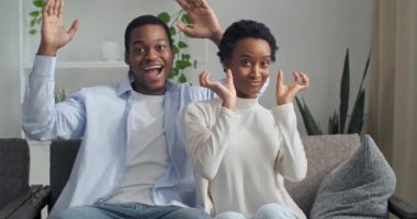 Aktif afro-amerikan çift, kanepede oturmuş birlikte somurtuyorlar, adam yüzücülerden gözlük yapıyor gözlerini elleriyle kapatıyor, kız kalp dansının şeklini gösteriyor.
