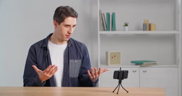 Zakenman freelance stylist zit aan tafel in huis records video voor vlog blog met behulp van mobiele telefoon, Kaukasische man praat over zijn uiterlijk en nieuwe shirt gesticulates legt uit aan smartphone camera — Stockvideo