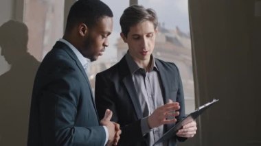 İki çok ırklı iş adamı Afro-Amerikalı erkek yönetici ve Kafkasyalı patron iş arkadaşları proje stratejisini tartışıyor, ofiste duruyor, belge sözleşmesi dosyalarına bakıyor, konuşuyor.