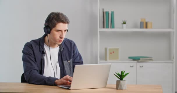 Caucasiano focado homem de negócios millennial cara sério estudante freelance usando fones de ouvido ouvindo música trabalhando remotamente na mesa no escritório em casa usando o serviço on-line para compras digitação navegação — Vídeo de Stock