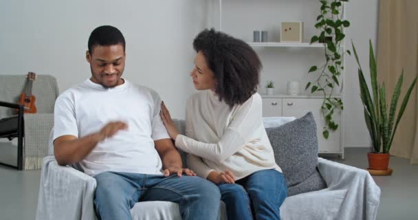 Afro american husband feeling stress while wife woman apologizing talking begging upset husband ask for forgiveness at home, girlfriend regrets consoles supports beloved boyfriend sitting on couch — Stock Video