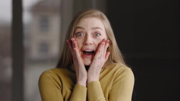 Porträtt av överraskad vinnare flicka blond kaukasisk tusenårig kvinna känner glädje från oväntade goda nyheter eller skvaller stänger munnen med händerna från chock undrar skrattar tittar på kameran — Stockvideo