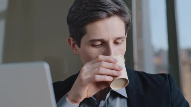 Pensive caucasian successful professional business man with laptop looking out window, dreaming, planning, thinking about ideas plans, drinking coffee, cocoa, tea from paper cardboard cup in office — Stock Video