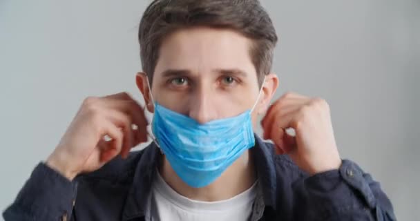 Portrait of caucasian millennial man teaches showing correct wearing of medical mask, close-up patient guy putting on respirator on his face closes mouth waving finger no covers nose shows thumbs up — Stock Video