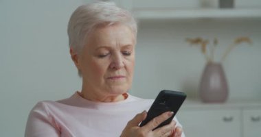 Ciddi odaklı Kafkasyalı yaşlı kadın akıllı telefon aramaları ekranına bakıyor arkadaşları telefon cihazları, modern teknoloji konsepti ve yaşlıları kullanarak uzaktan alışveriş siparişi veriyor.