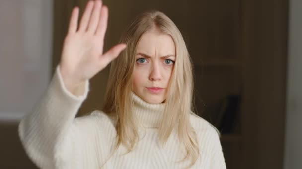 Portrait of offended blonde caucasian woman makes stop gesture with her palm forbidding waving head no. Young girl in white sweater looking at camera demonstrates refusal putting hand in front of her — Stock Video