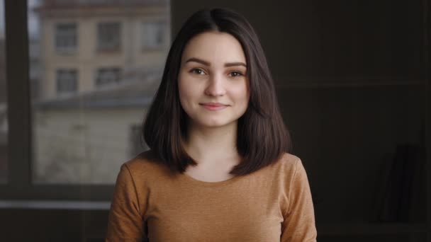 Portrait of lonely happy cute teenager girl standing indoors posing in room looking at camera. Close-up caucasian millennial friendly brunette woman smiling with calm carefree female face expression — Vídeo de stock