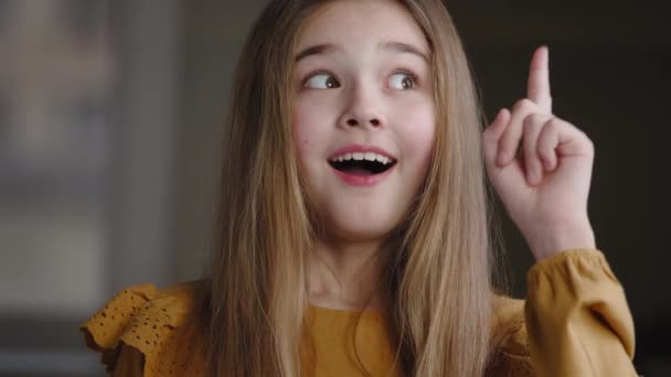 Close-up portrait of female face child, creative schoolgirl teenager pupil comes up with idea plan makes insight gesture. One blonde girl raising index finger up smiling satisfied looks at camera — Vídeo de Stock