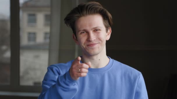 Porträt des jungen kaukasischen Typen Millennial männliches Model Teenager trägt blaues Sweatshirt stehend, posiert macht Geste hey Sie, zeigt Zeigefinger in die Kamera, hebt den Daumen nach oben, Symbol der Übereinstimmung — Stockvideo