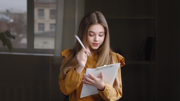 Portret kreatywnej dziewczynki nastolatka uczennica biały mądry córka stoi sam w pokoju w domu na tle okna trzymając folder z papieru wymyśla plan pisania notatki — Wideo stockowe