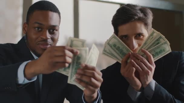 Retrato de dos empresarios exitosos multiétnicos gerente afroamericano y ejecutivo caucásico sostienen dinero mostrando dólares a la cámara se regocijan en triunfo éxito celebran lanzamiento de billetes en el aire — Vídeos de Stock