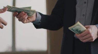 Çoklu etnik çeşitlilikte tanınmayan iki iş ortağının yakın plan fotoğrafı. Para geliri paylaşımı. Dolar sayan erkek eller iş arkadaşına maaş verir. Uzman, minnettarlığını tokalaşarak ifade eder.