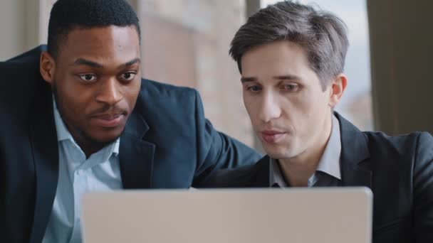 Två multietniska vuxna kollegor tittar på laptop i ämbetet. Kaukasiska affärsman råder afro amerikansk chef anställd diskuterar projekt eller problem med online-tjänst app med hjälp av dator — Stockvideo