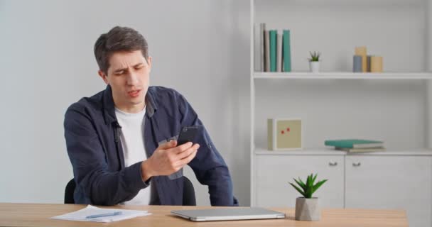 Un homme millénaire caucasien assis à la table au bureau à la maison parlant dans la caméra Web de téléphone mobile faisant conférence de chat vidéo en ligne sur Internet utilise un smartphone sans fil moderne pour communiquer — Video