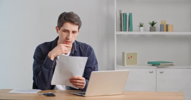 Concentrated caucasian millennial businessman sitting at home desk or in office, looking at documents, reading letter paper, looking in financial statement, receiving notice from bank, doing paperwork — Stock Video