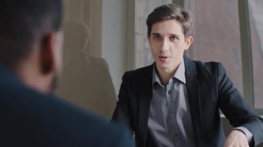 Caucasian professional male business man expert advice talking consulting unrecognizable afro american client customer investor sitting back to camera about financial investment on meeting in office