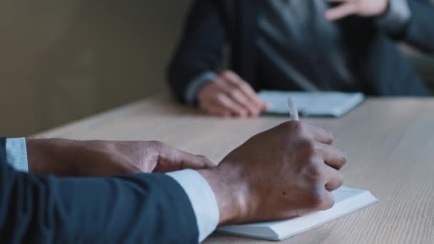 Close-up male hands of multiethnic business men negotiating discussing strategy project plan sitting at office table, Afro American employee writes notes in notebook listening to Caucasian man — Vídeos de Stock