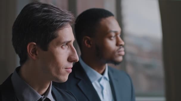 Portrait of two multiracial business men human stand in profile in modern office, Caucasian boss and African American man employee look out window pensive thinking about problem of company planning — Video