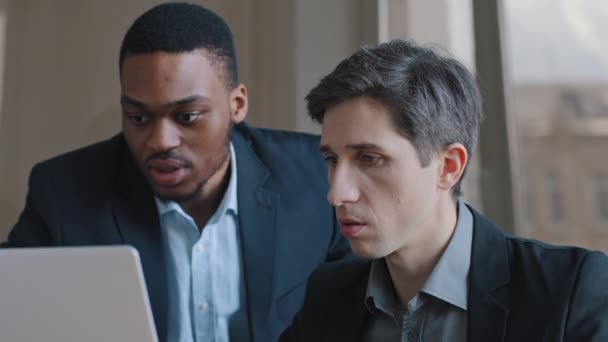 Serious two male business men discuss project, caucasian man expert advice software pointing on laptop consulting african manager trainee about computer app explains shows corporate services at office — Αρχείο Βίντεο