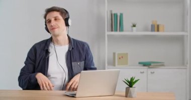 Neşeli, mutlu iş adamı, beyaz adam, ofiste dizüstü bilgisayarlı, kablosuz kulaklık takıyor, müzik dinliyor, kulaklık takıyor, dans ediyor, ses parçalarıyla eğleniyor.