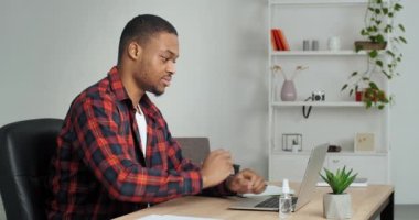 Evde dizüstü bilgisayar ve not defteri kullanarak üniversite ödevi yapan Afrikalı Amerikalı öğrenci verileri analiz ediyor hesaplamalar yapıyor notlar yazıyor, planlar yazıyor.