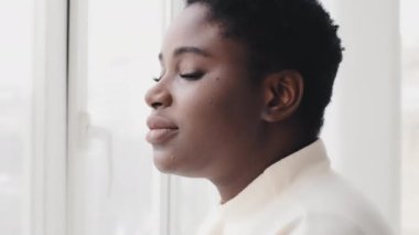 Kadın portresi, Afro-Amerikalı mutlu kız pencerenin kenarında durup geniş dişli beyaz dişlerle gülümseyen kameraya bakıyor. Afro etnik siyah güzel milenyum kadını şeffaf camın yanında poz veriyor.