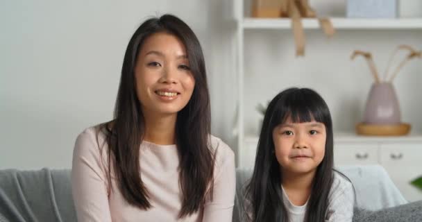 Азиатская мать с маленькой дочерью девочка смотрит на веб-камеру размахивая руками, говоря привет, общаясь через онлайн чат конференций делает интернет-звонок из домашней записи видео для блога — стоковое видео