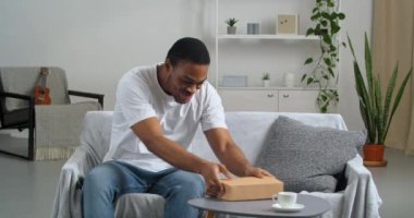 Mutlu Afro-Amerikalı adam gündelik kıyafetler giyiyor çevrimiçi mağazalardan gelen postayla paketler alıyor. Kutuları açıyor, karton kutuları açıyor, gri defter okuyor, edebiyat okumaktan zevk alıyor.